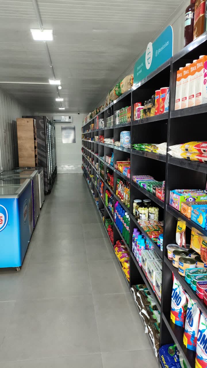 Corredor interno de loja em container, com gôndolas cheias e freezers