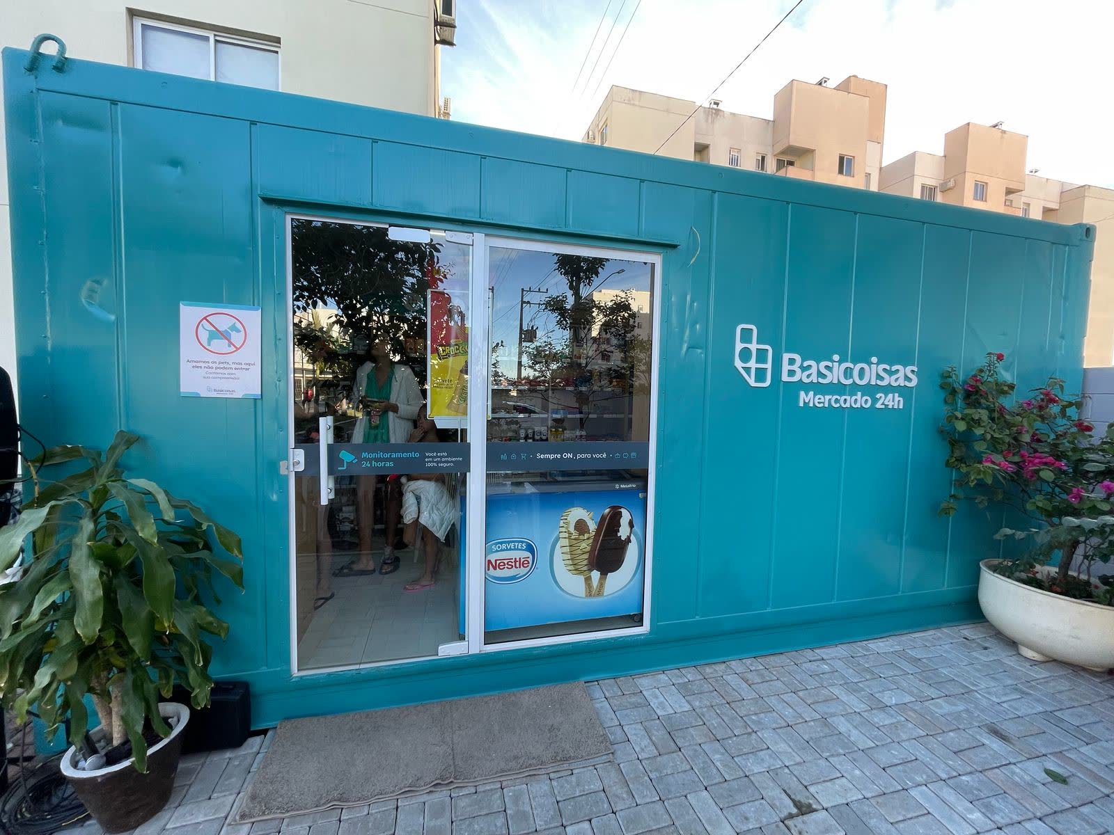 Fachada de loja Basicoisas em container turquesa, com porta de vidro